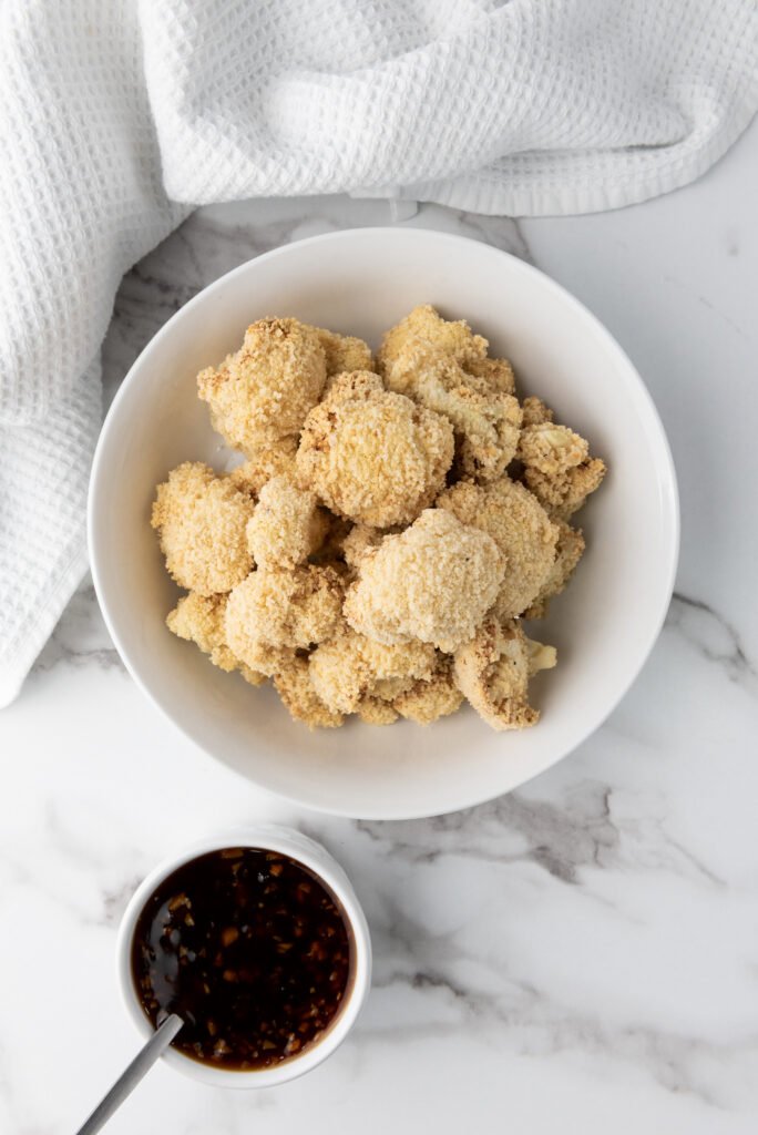 Coat the Wings & Garnish 🌟-Crispy teriyaki-glazed cauliflower wings served on a plate with sesame seeds and green onions.