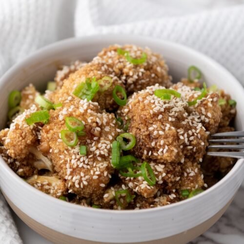 Crispy teriyaki-glazed cauliflower wings served on a plate with sesame seeds and green onions.